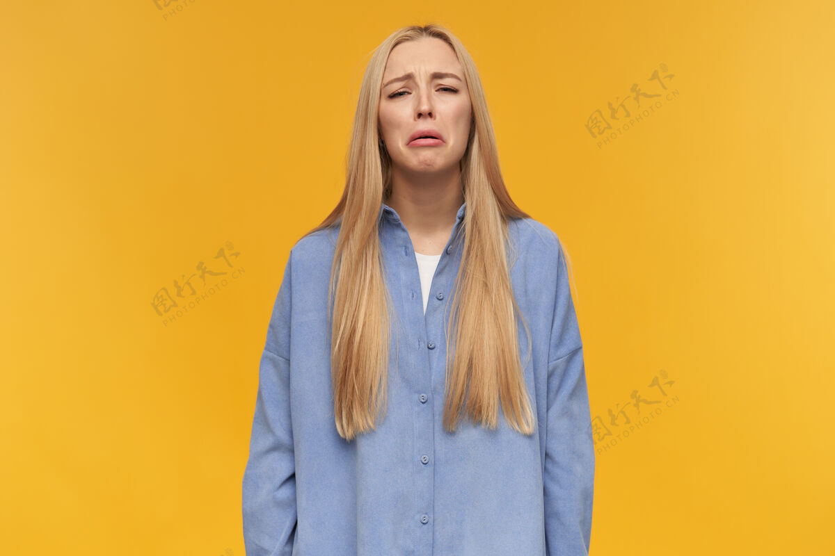 面部十几岁的女孩 金色长发哭泣的女人穿着蓝色衬衫人和情感的概念非常难过的事情 哭泣看着镜头 孤立在橙色背景下皮肤成人20多岁