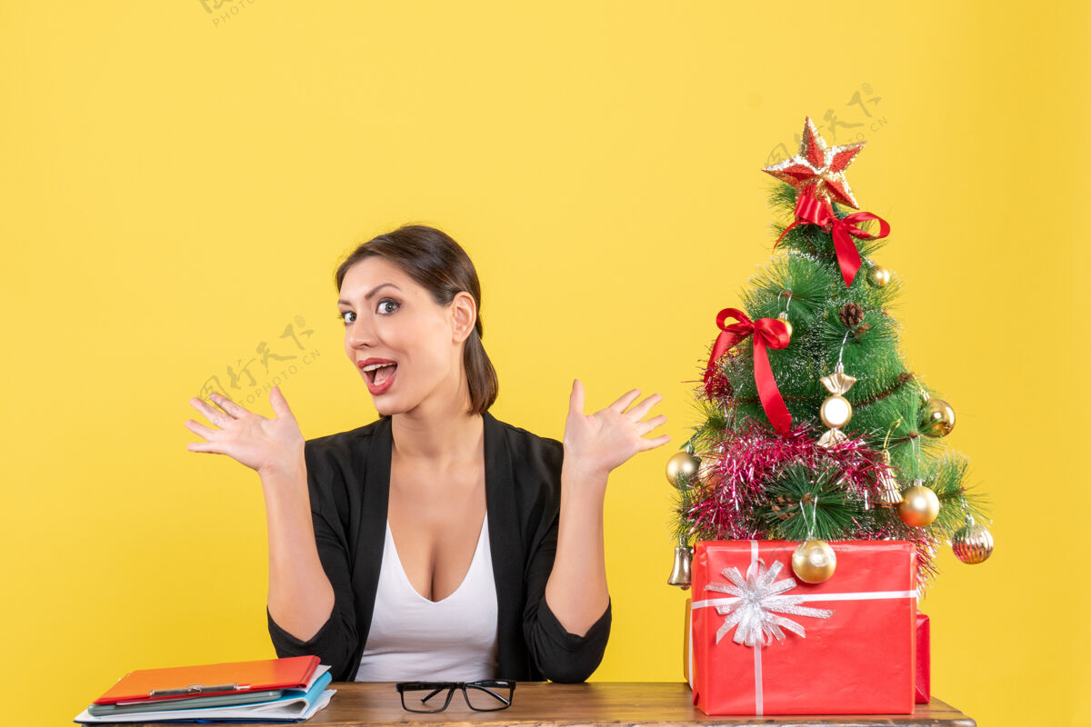 欢呼新年心情与惊喜的年轻女子装饰圣诞树在黄色的办公室树年轻的女人黄色