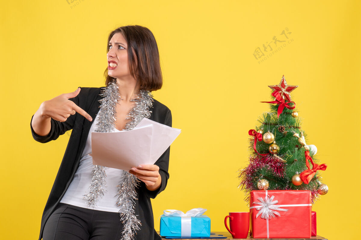 头发圣诞节的心情与困惑美丽的女士站在办公室和指向文件在办公室的黄色黄色快乐黑发