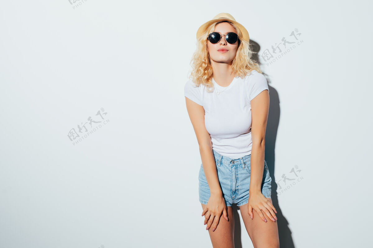 玩一个微笑迷人的女人的肖像 戴着太阳镜 夏装 戴着帽子 孤立地站在白色的墙上时尚人夏天
