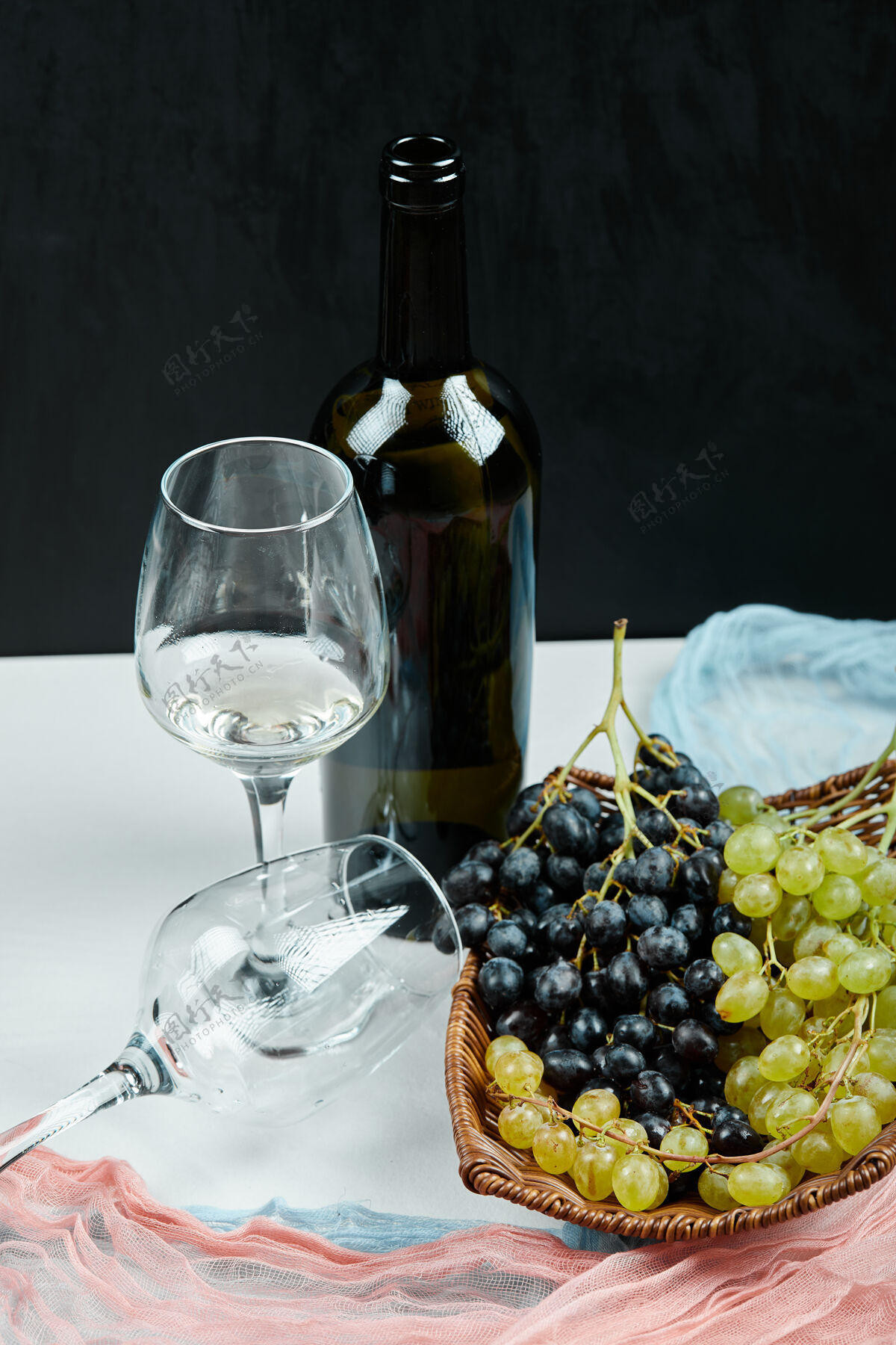 潮湿篮子里放着一簇混合的葡萄 还有一杯葡萄酒和一瓶粉色和蓝色的桌布高质量的照片成熟叶子一串