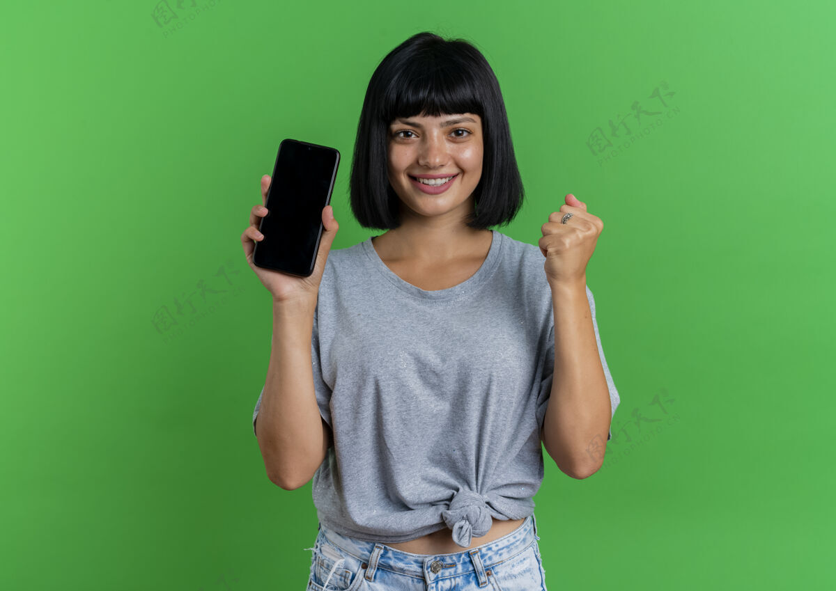 复制微笑的年轻黑发白人女孩手持电话 将拳头隔离在绿色背景上 留有复印空间拳头空间持有