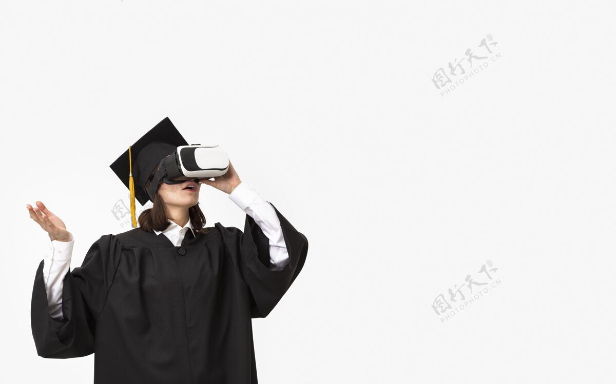 设备穿着毕业礼服戴毕业帽戴着虚拟现实耳机的女人仿真技术虚拟现实