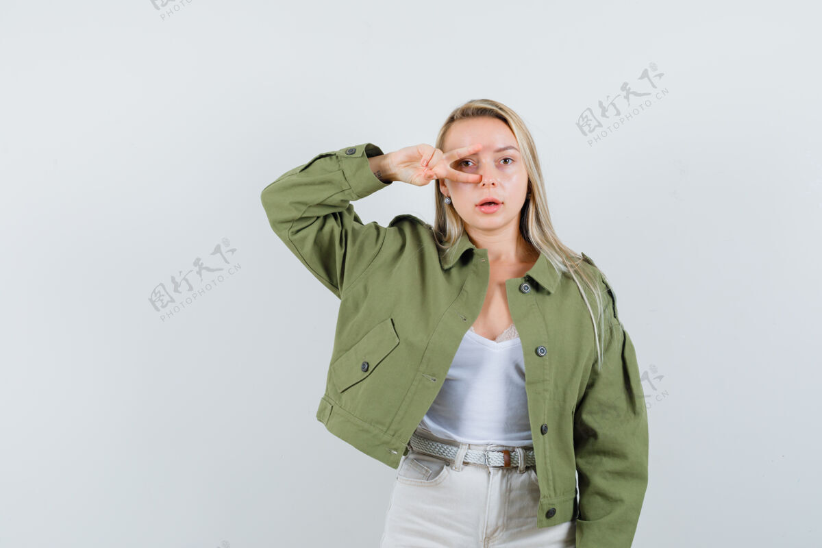 健康穿着夹克衫 衬衫 前视图的年轻女性在眼睛上方显示v形标志年轻夹克皮肤