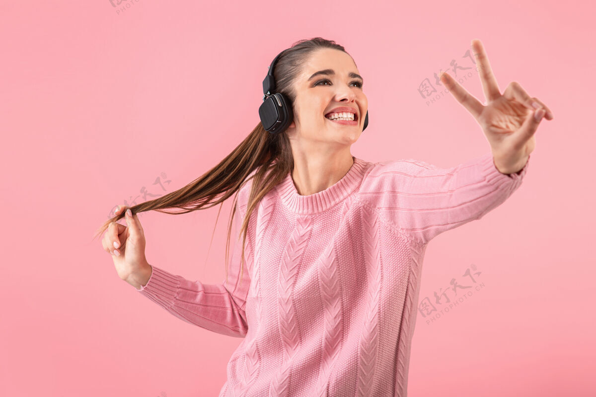 无线年轻漂亮的女人戴着无线耳机听音乐 穿着粉色毛衣微笑着立体声欢呼女士