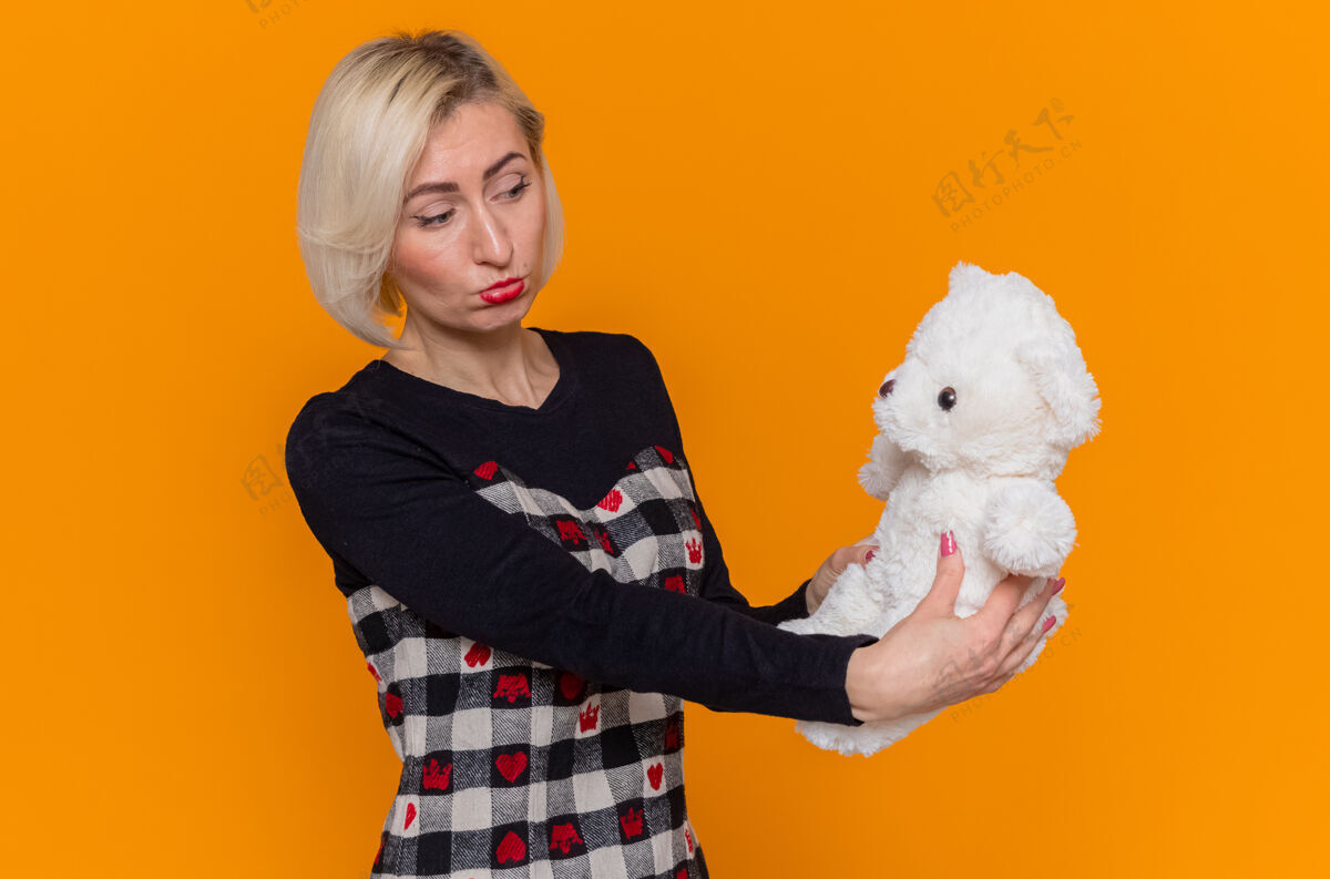 美丽不高兴的年轻女子拿着泰迪熊作为礼物看着它悲伤的表情熊不高兴年轻