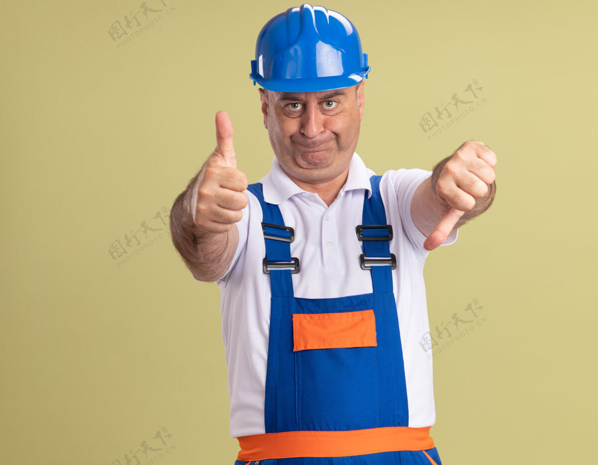 成人自信的成年建筑工人穿着制服 竖起大拇指 竖起大拇指 竖起大拇指 孤立地站在橄榄绿的墙上向下站立人