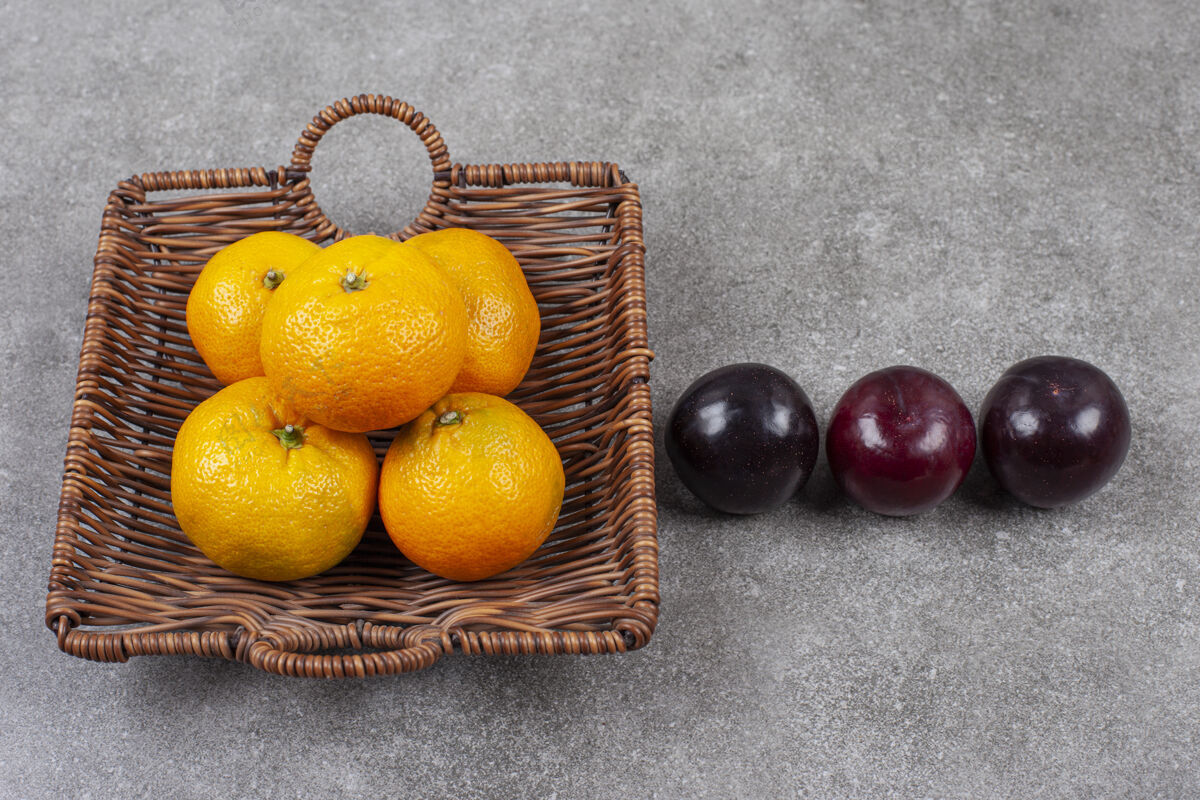餐桌柳条篮子上放着新鲜的甜橘子和李子柳条柑橘有机