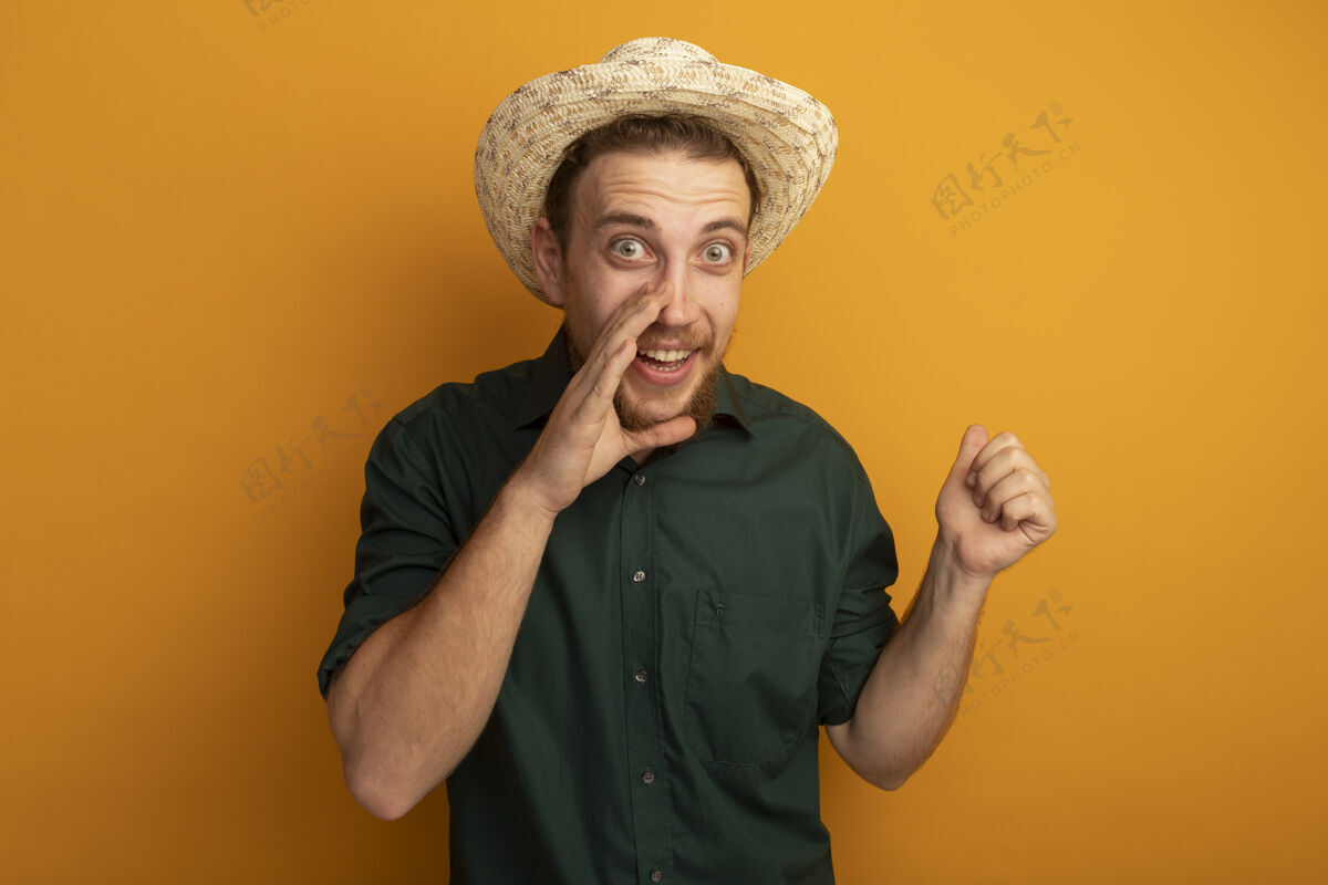 男人兴奋的金发帅哥 戴着沙滩帽 手紧挨着嘴 把拳头孤立在橙色的墙上人金发姿势