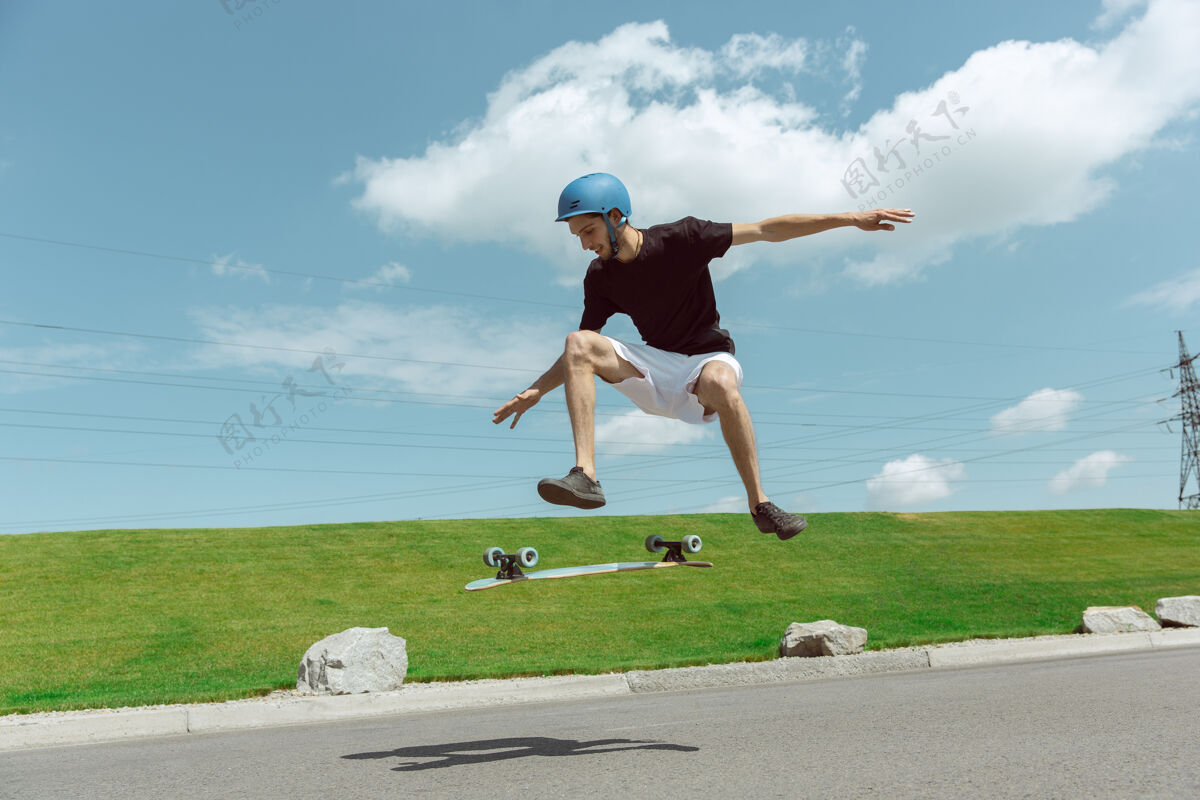 人在阳光明媚的日子里 在城市街道上玩滑板的人年轻人在草地附近骑马 玩长板休闲活动 运动 极限 爱好和运动的概念运动空气滑板