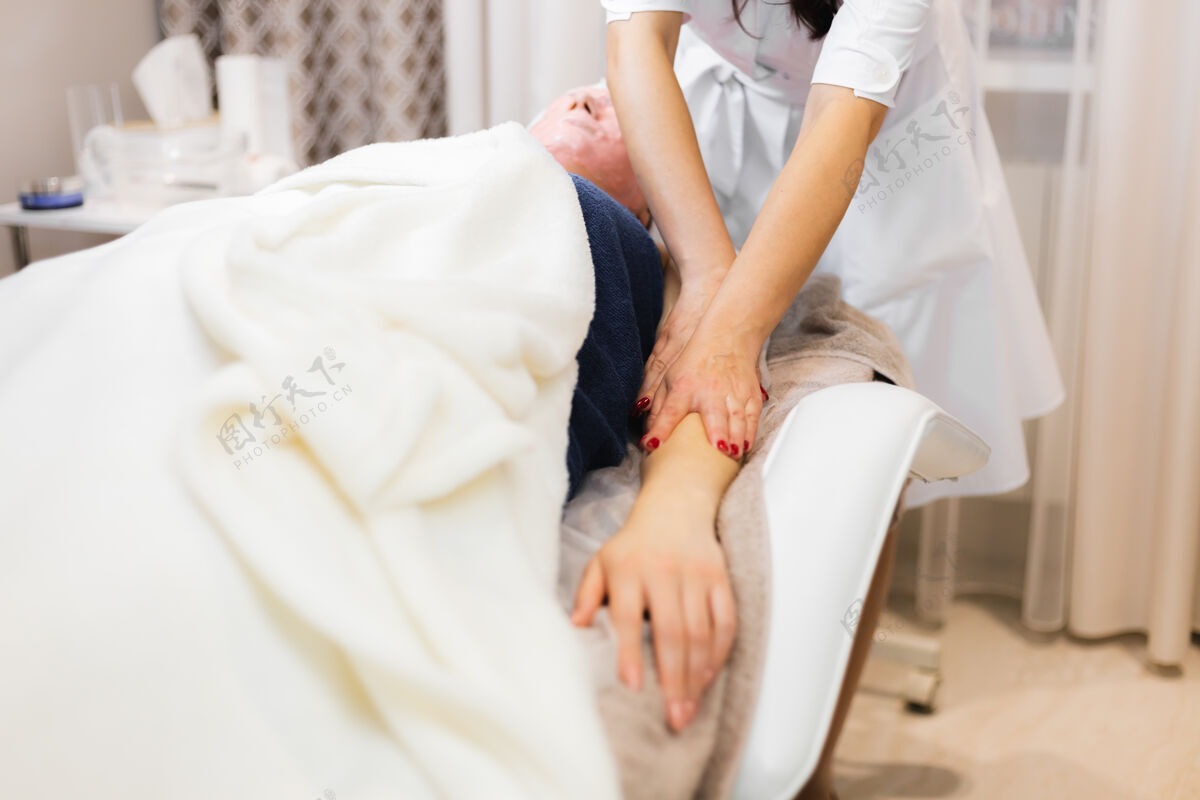 健康一位年轻的女顾客脸上戴着海藻酸钠面膜 躺在美容台上 美容师做手工按摩皮肤科女性治疗