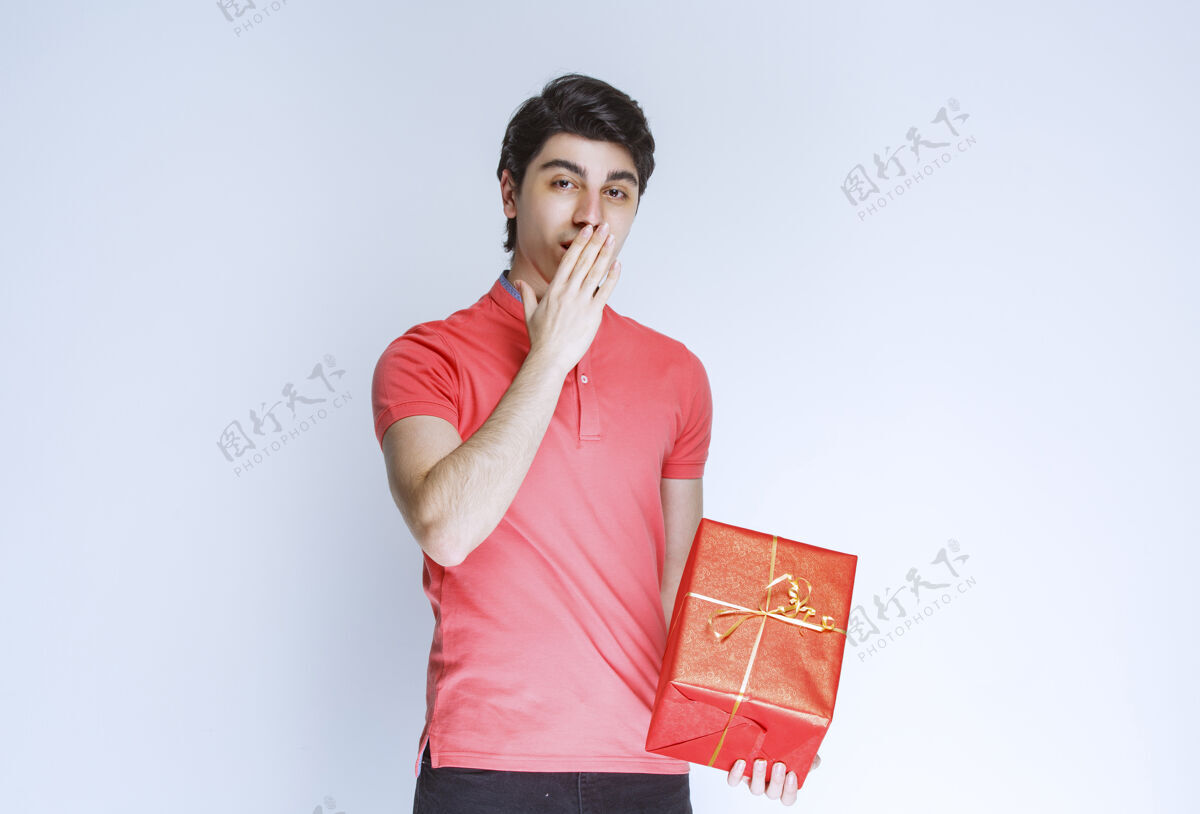 困惑拿着红色礼盒的男人把手放在嘴边思考着聪明年轻休闲