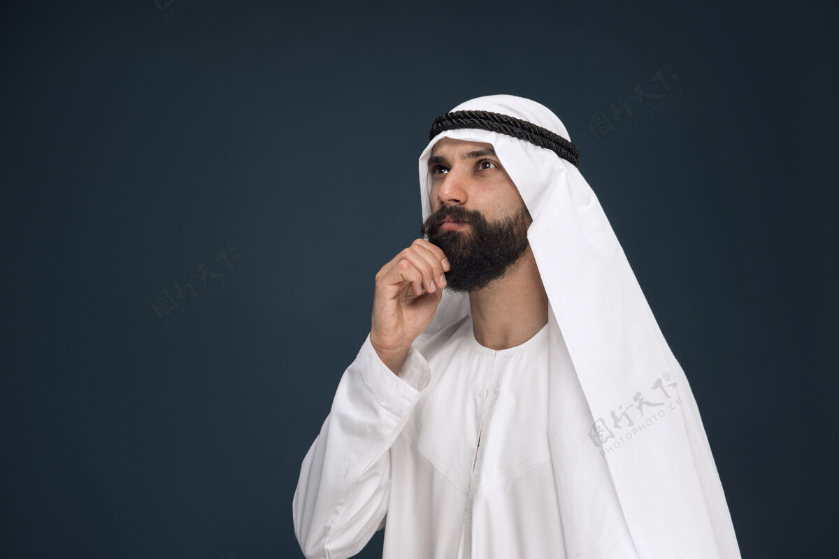 深蓝色工作室背景上的半身阿拉伯沙特商人肖像年轻的男模站着 看起来很体贴商业 金融 面部表情 人类情感的概念震惊搞笑面部