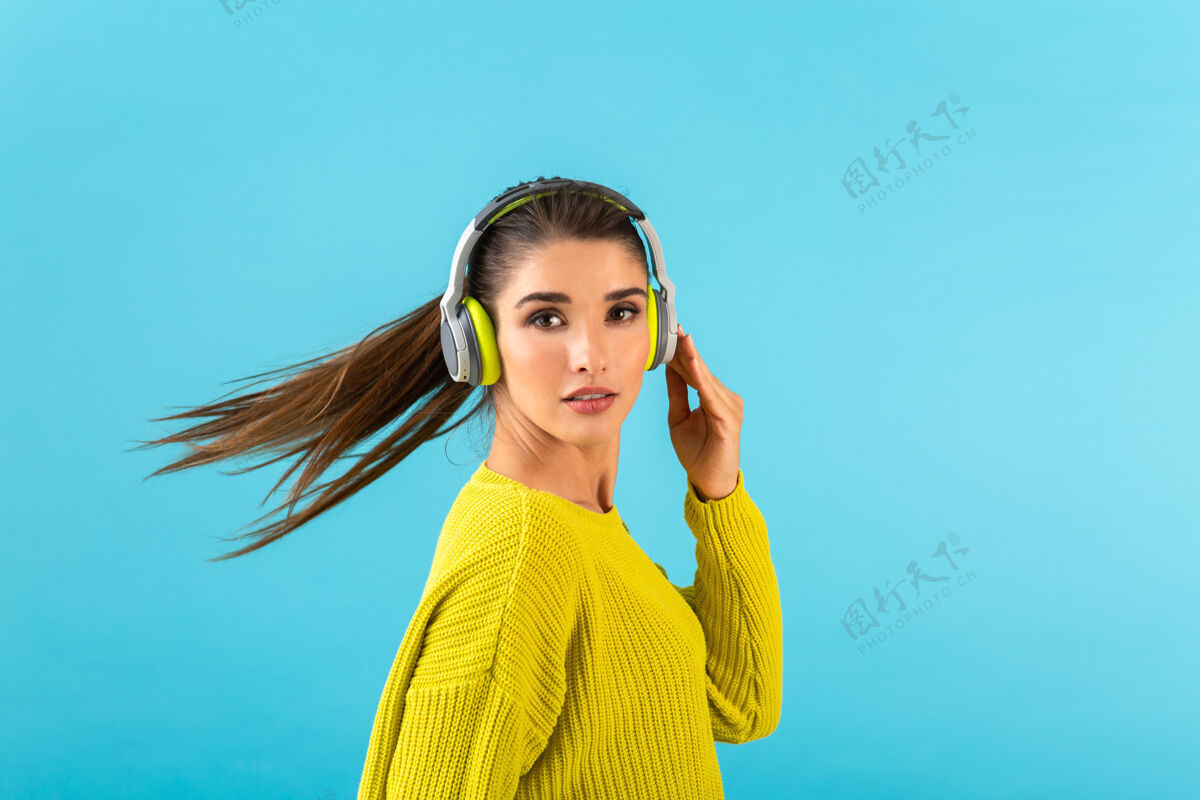 微笑迷人时尚的年轻女子戴着无线耳机听音乐快乐地穿着黄色针织毛衣乐趣模特女人
