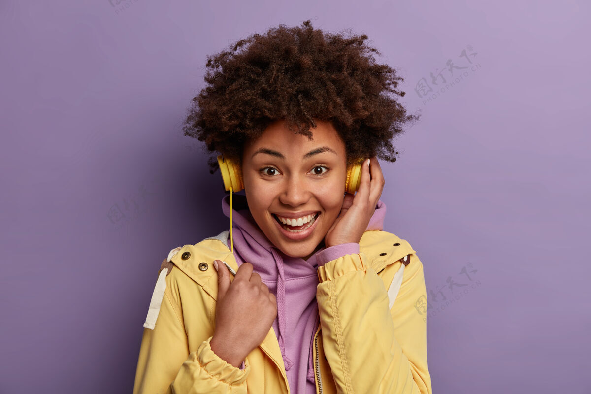 放松独立拍摄的乐观卷曲时髦女孩享受积极的旋律在电子耳机 听音乐通过现代耳机头像连帽衫卷发
