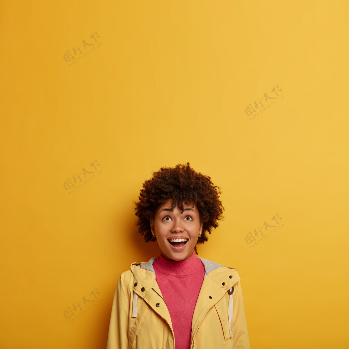 情绪快乐大笑的女人兴致勃勃地看着上面 看看有趣的广告 穿着休闲夹克 卷发 对着黄色的空间摆姿势女性无领姿势