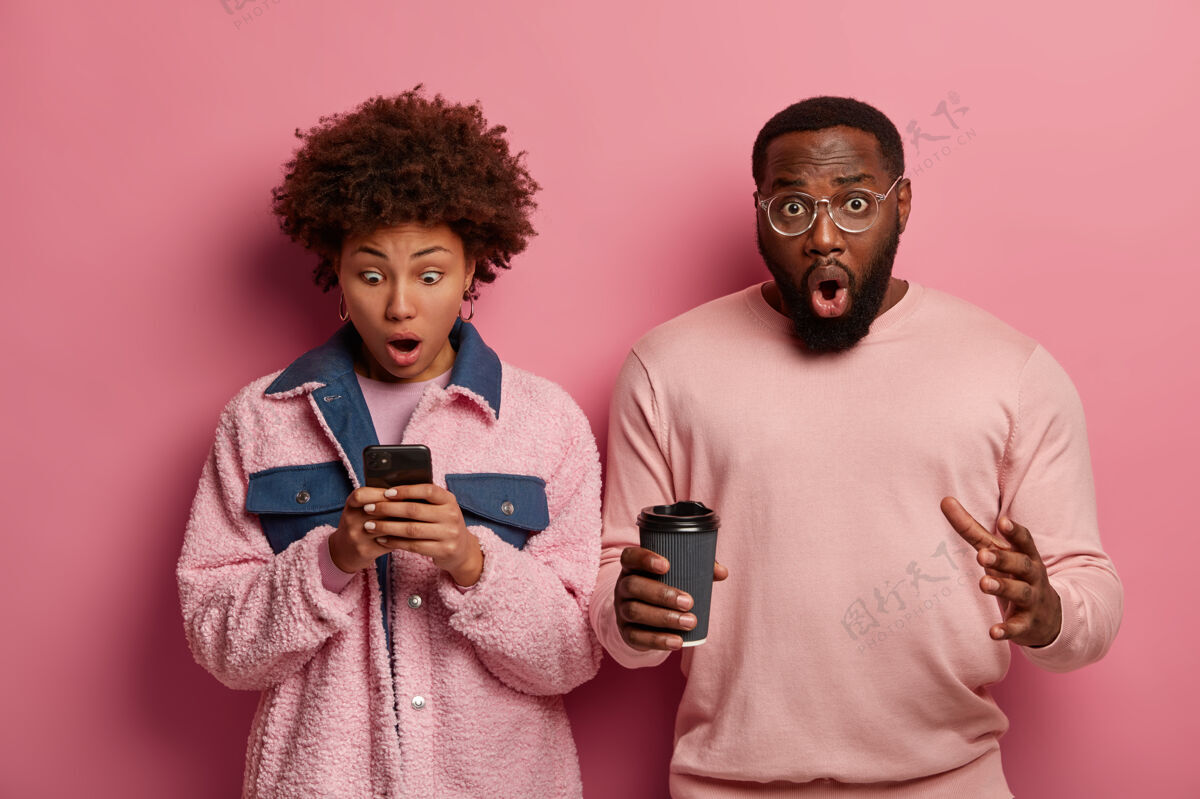 胡须惊呆了情绪化的女人盯着智能手机显示屏 收到奇怪的短信 惊讶的大胡子男人喝外卖咖啡非洲手机可怕的