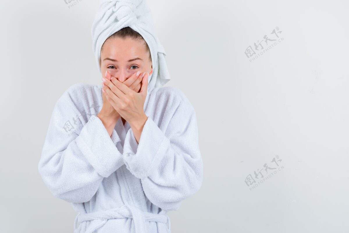 魅力年轻的女士手放在嘴上 穿着白色浴衣 拿着毛巾 看起来很开心正面图前面亚洲人完美