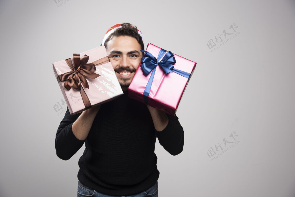 礼物一个戴着圣诞老人帽子的笑脸男人 手里拿着新年礼物帽子蝴蝶结年轻人