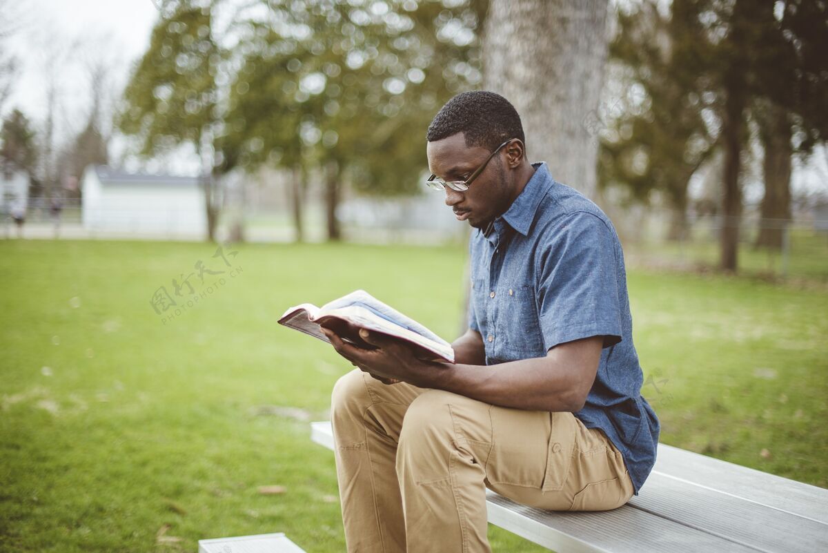 基督徒年轻的非洲裔男性坐在长椅上读圣经公园男性长凳