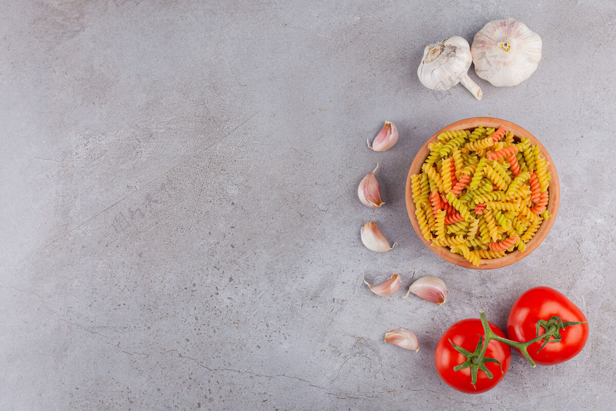 桌子一碗五颜六色的生螺旋意大利面 配大蒜和新鲜的红色西红柿自然面食视图