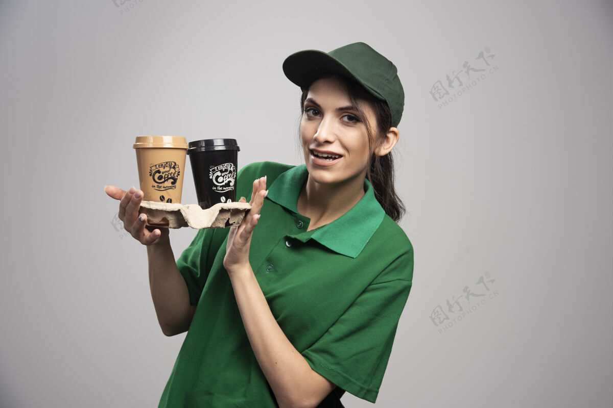 女性穿着绿色制服的女送货员拿着咖啡摆姿势送货快递制服