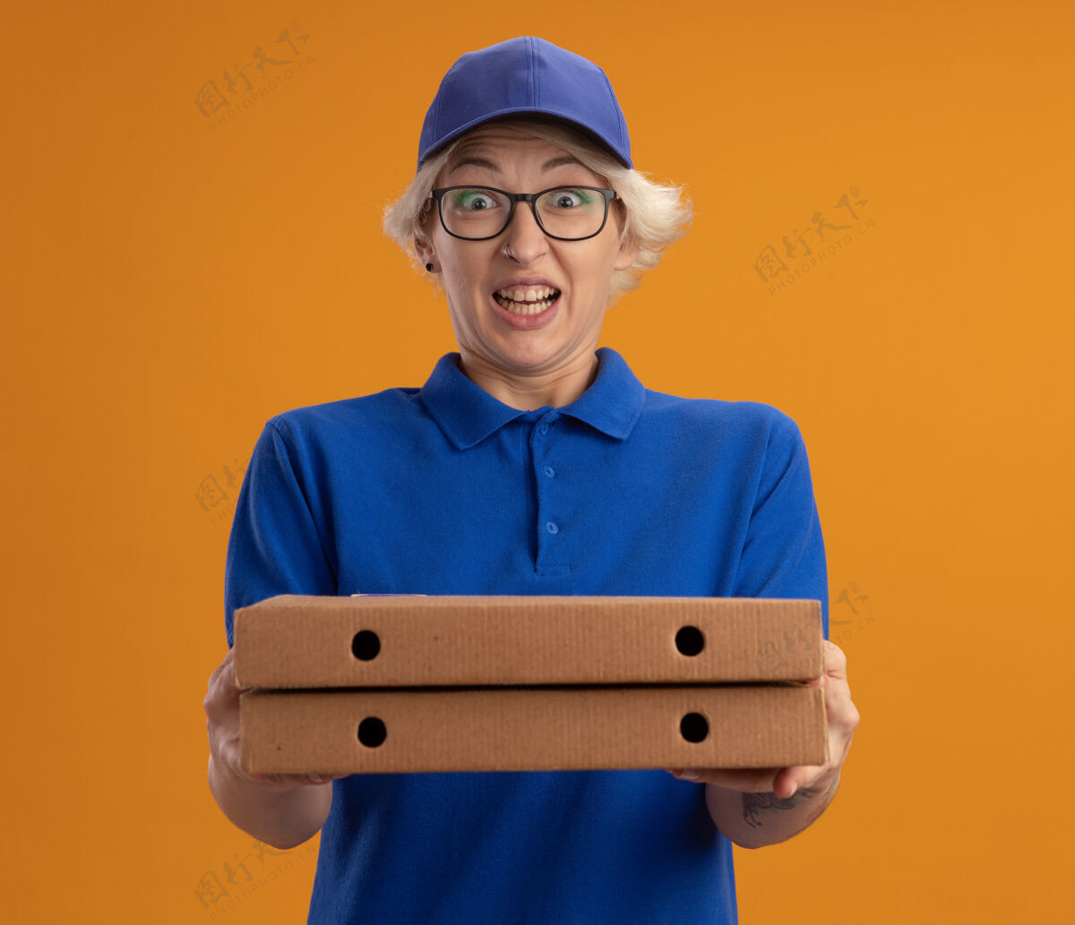 兴奋身穿蓝色制服 戴着眼镜 拿着比萨饼盒的年轻送货员在橙色的墙上兴奋而快乐女人盒子送货