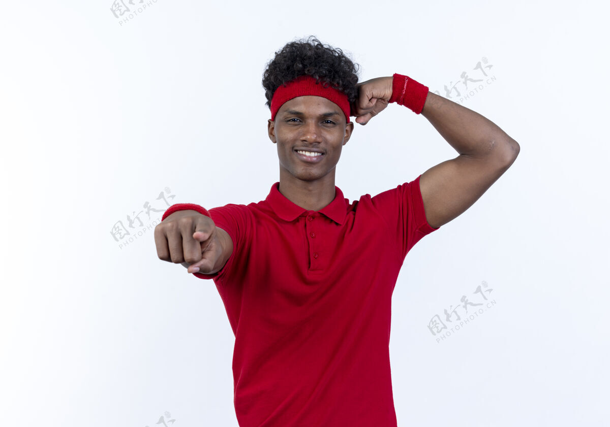 年轻高兴的年轻黑人美国运动男子戴头带和腕带显示您的手势和做强烈的手势隔离在白色背景运动姿态表演