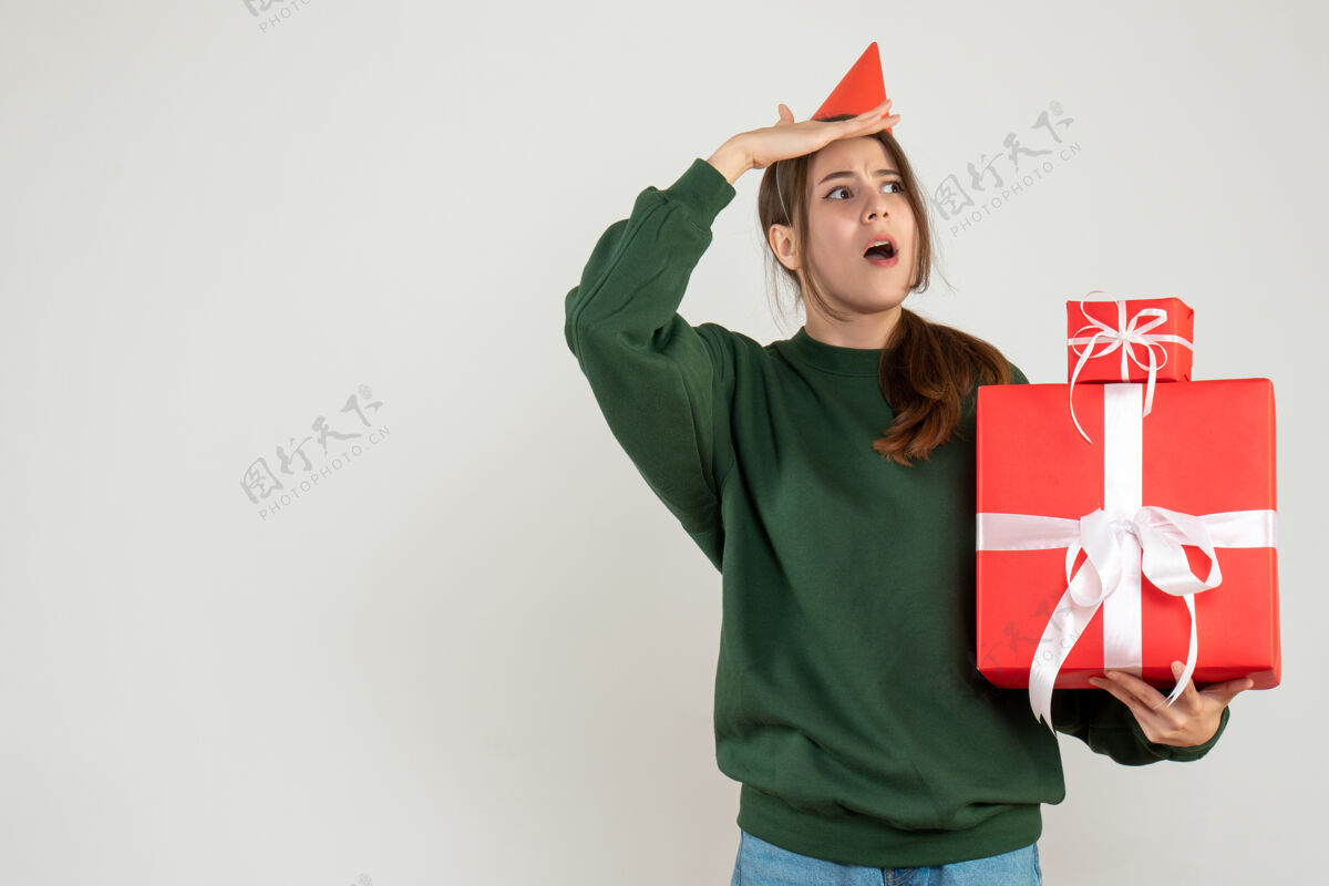 礼物正面图好奇的女孩戴着派对帽 手里拿着她的圣诞礼物美丽举行圣诞节