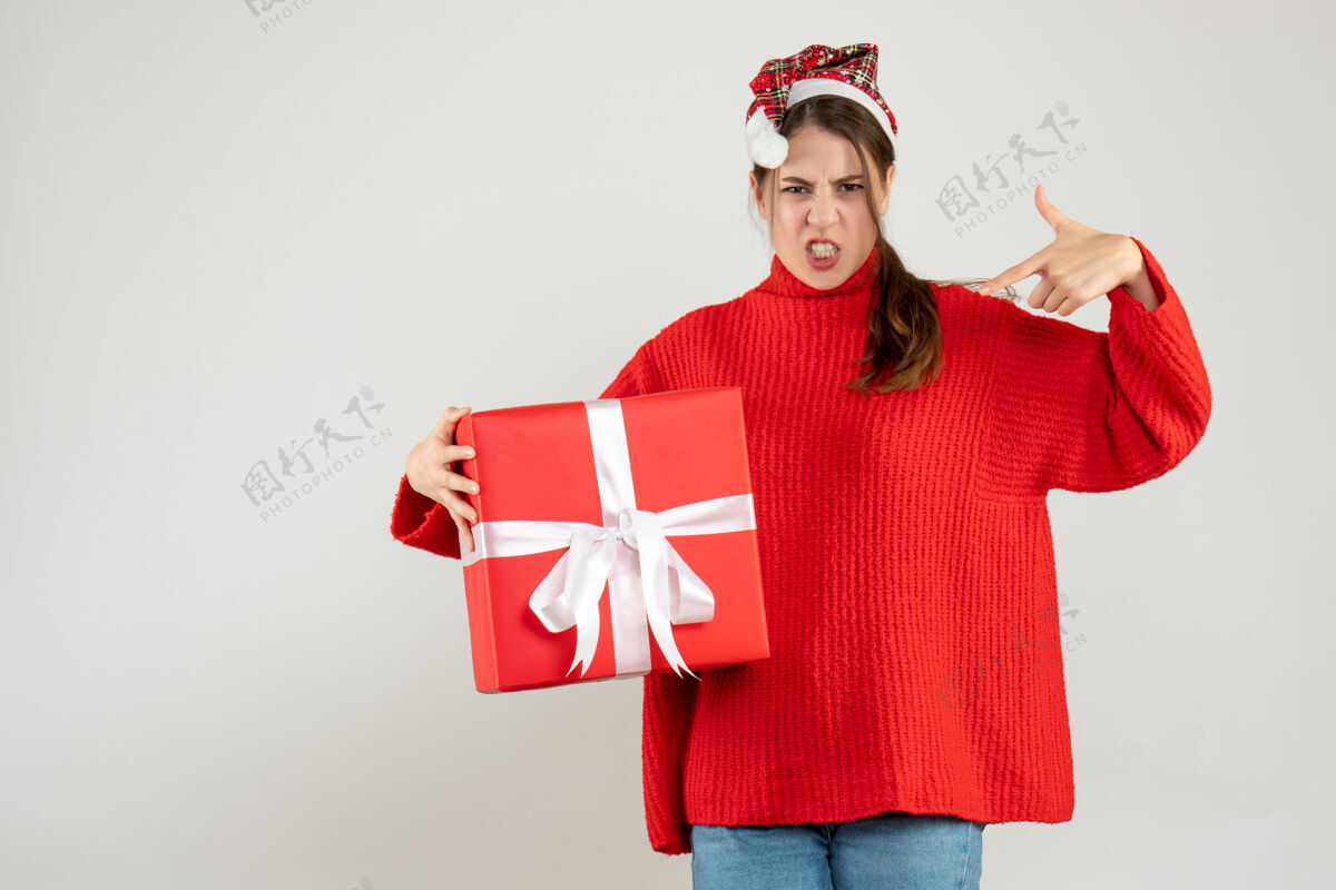 工作前视图愤怒的女孩拿着圣诞帽拿着礼物指着自己手手指帽子