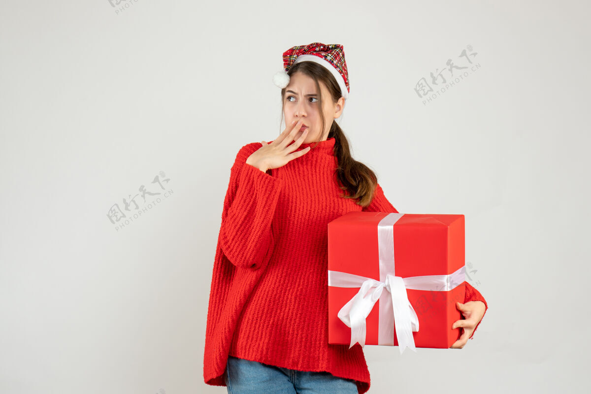 帽子前视图困惑的女孩戴着圣诞帽拿着礼物放在手上圣诞老人人礼物