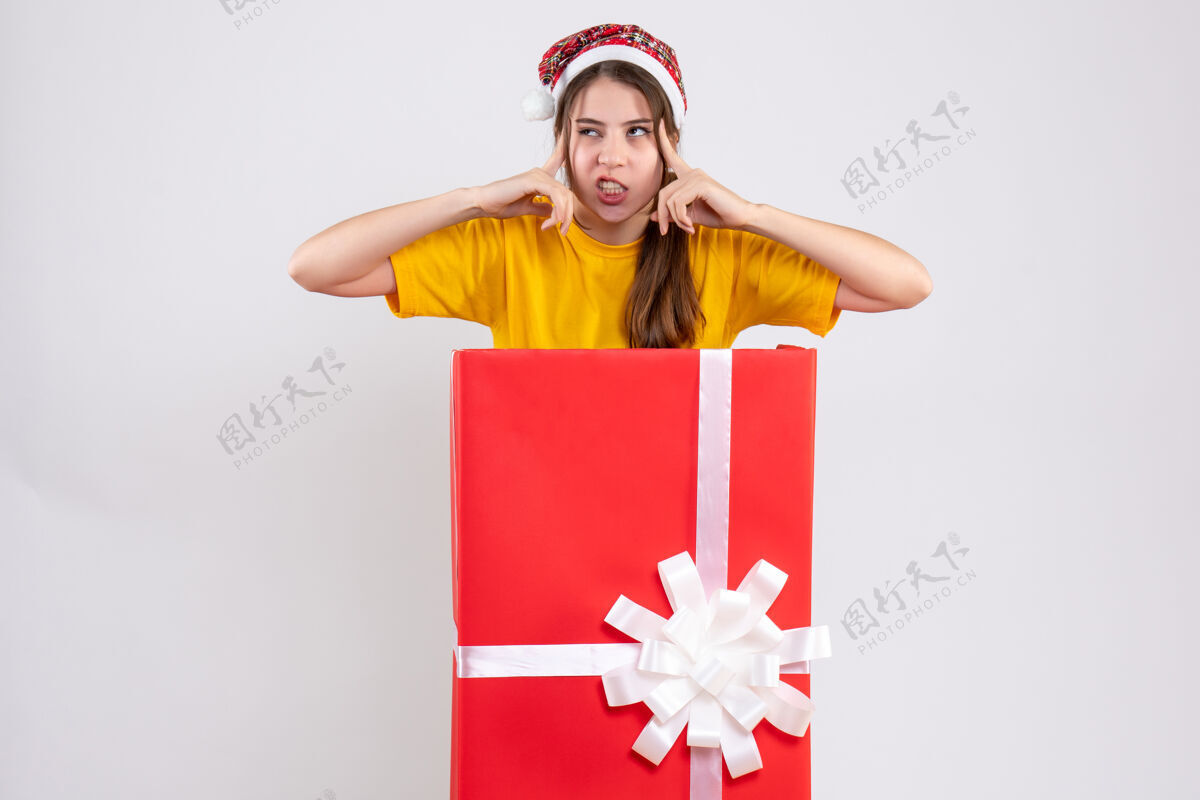 圣诞老人前视图愤怒的女孩戴着圣诞帽站在大圣诞礼物放手指后面漂亮人寺庙
