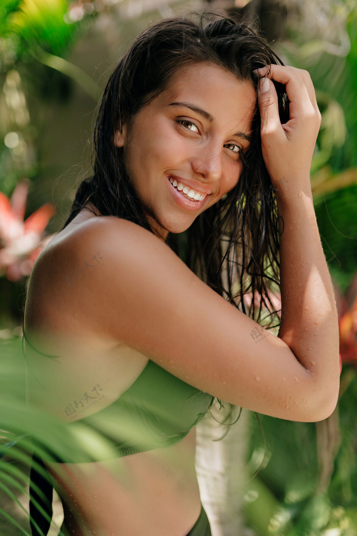 微笑这张照片是一位年轻迷人的棕褐色女子的肖像 她深色的湿头发在异国植物的背景下微笑着对着镜头摆姿势孤独天堂皮肤