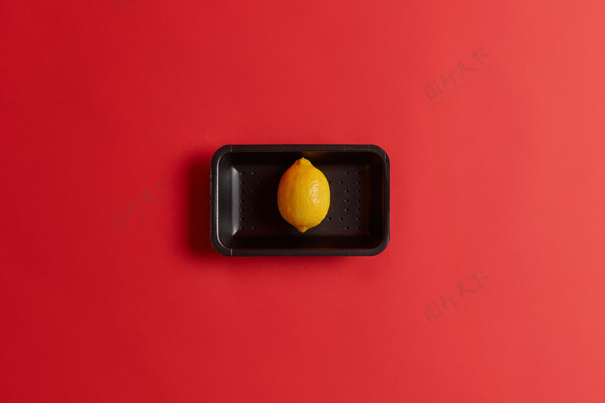 活力在超市购买的黑色托盘上放着新鲜成熟的黄色单柠檬的照片 红色背景下隔离开来整个奇异的水果含有大量维生素c是烹饪夏季冷柠檬水的原料新鲜热带柠檬