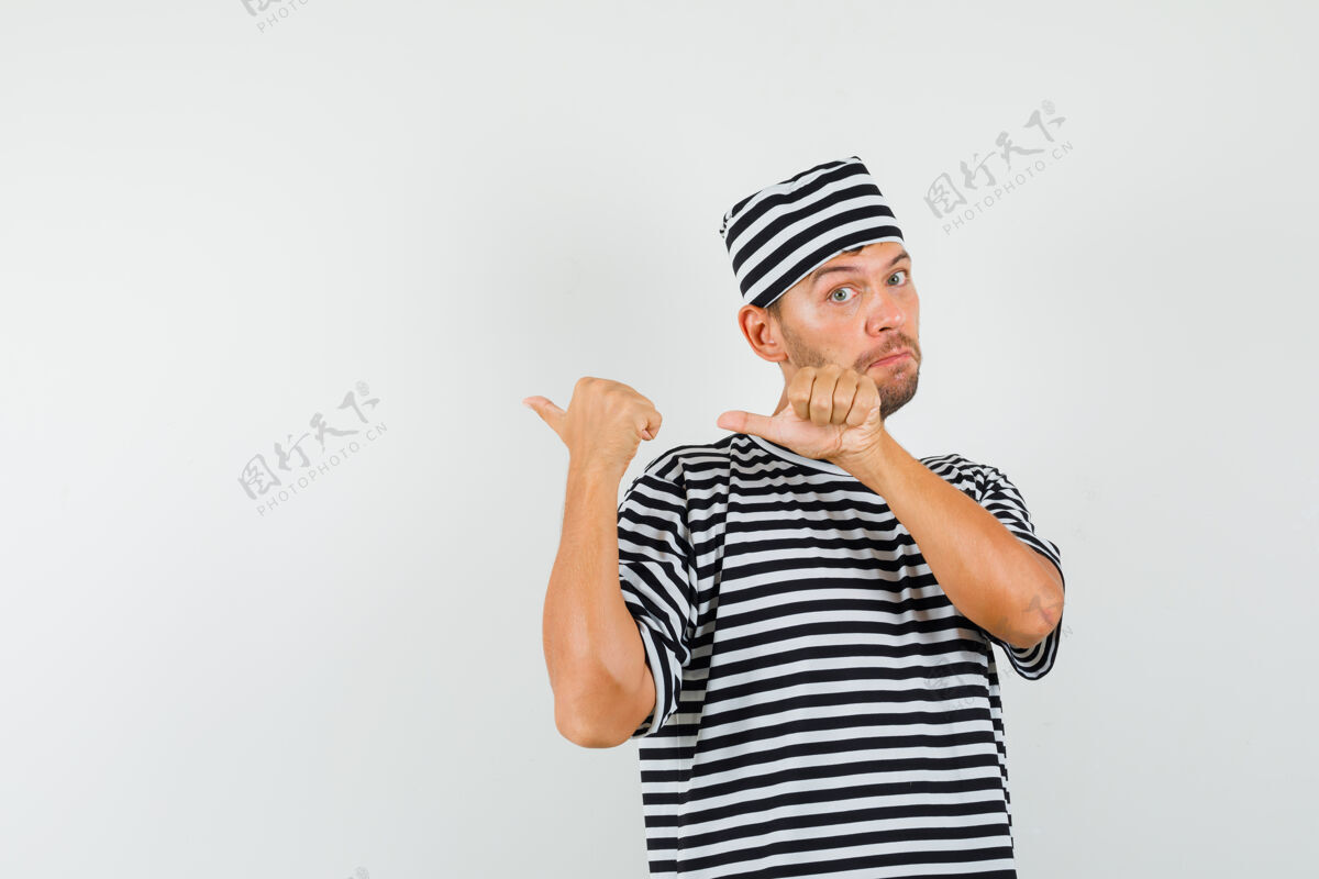男人戴着条纹t恤帽子的年轻人用拇指指着后面 看上去很困惑休闲帽子手指
