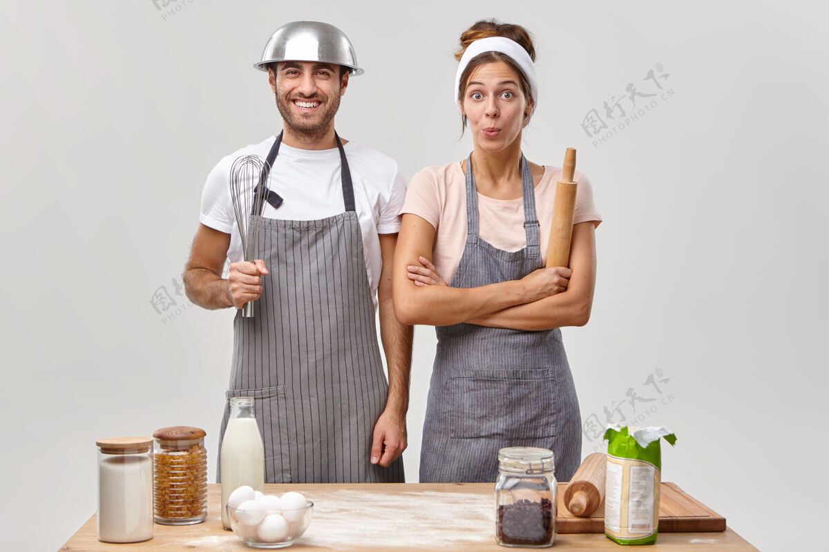 女人快乐的已婚夫妇在烹饪比赛中 做美味的饭菜 站在一起 穿着围裙 拿着厨房用品 一边准备糕点一边玩烹饪挑战概念家庭搅拌鸡蛋