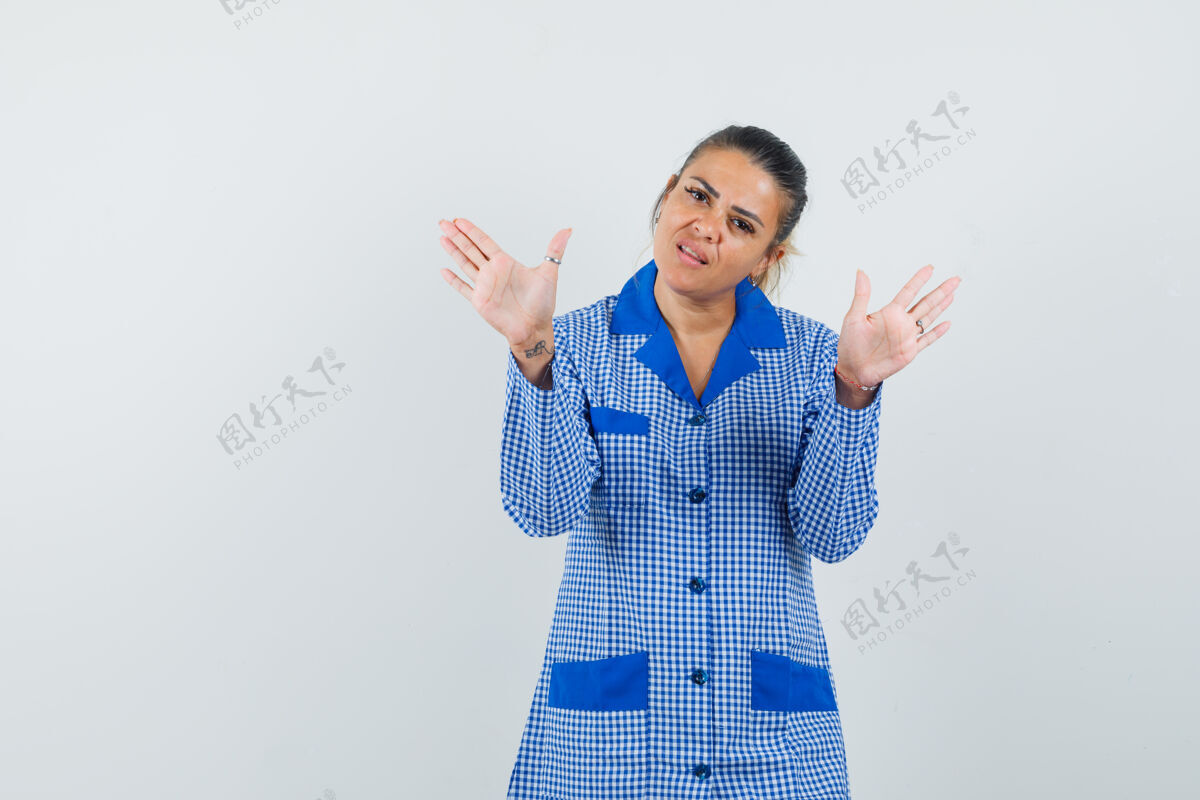 肖像年轻女子站在投降的姿势在蓝色格子睡衣衬衫 看起来很漂亮前视图人漂亮投降