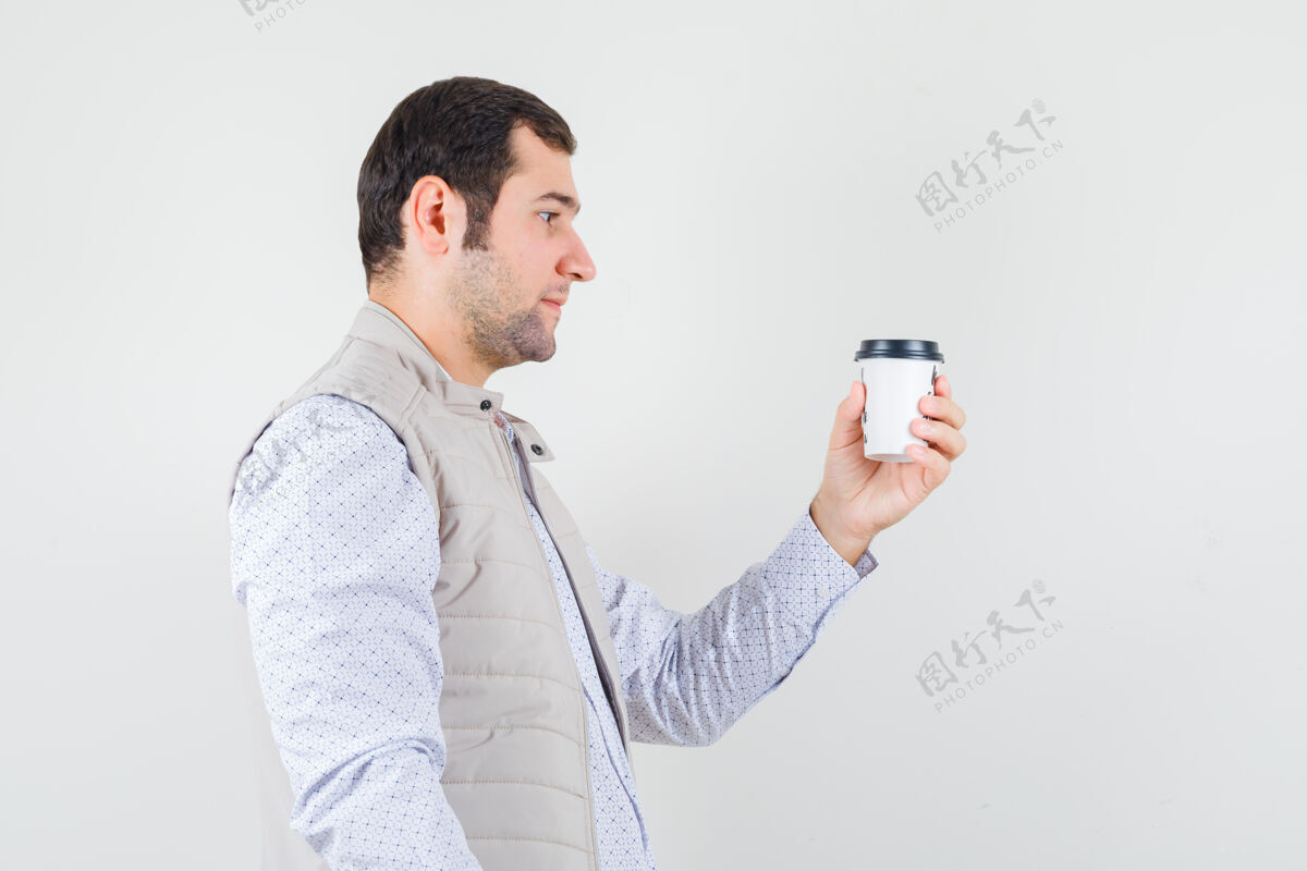 男性年轻人手里拿着一杯外卖咖啡 穿着米色夹克看着它 神情严肃 正面照杯子咖啡模特
