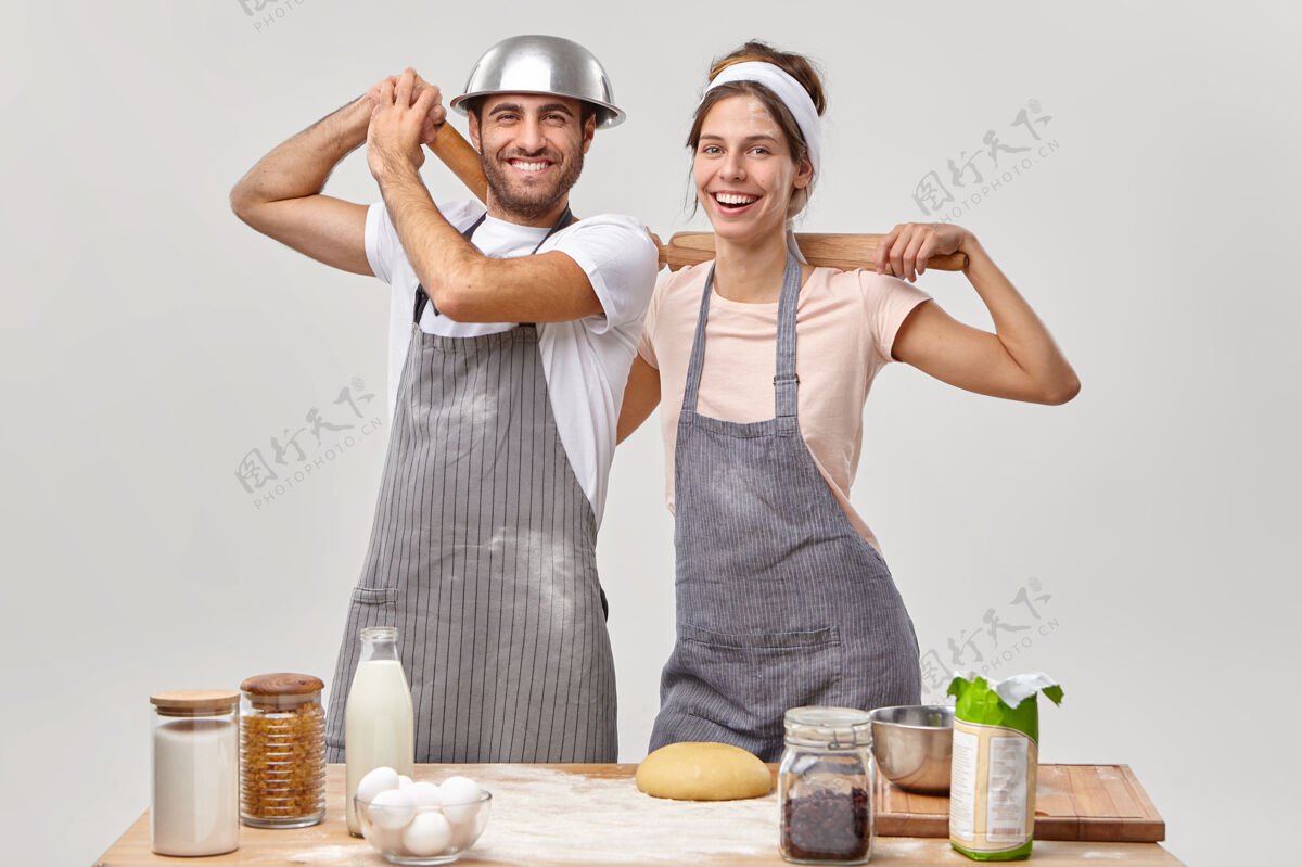 忙碌积极满意的夫妇站在厨房桌子旁边 用擀面杖做面团 烤饼干糕点 玩得开心 穿上沾满面粉的围裙呆在家里做饭美味自制活动
