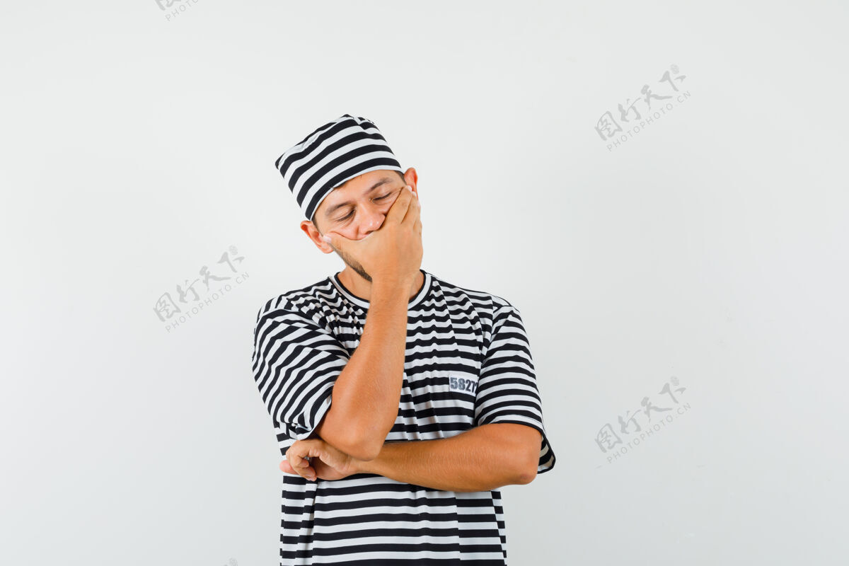 男性年轻的男性手放在嘴上 戴着条纹t恤帽子 看起来很困人胡须手