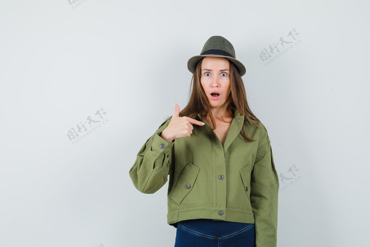惊喜年轻的女士指着自己的夹克裤子帽子 看起来很惊讶连衣裙积极女士