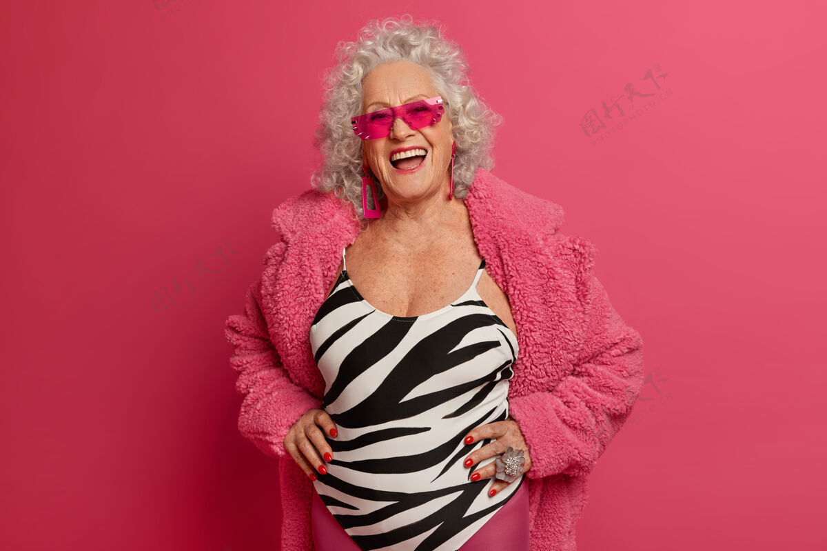 站快乐无忧无虑的熟女画像心情好 享受生活 谈吐愉快 戴着时髦的太阳镜 对着粉色的墙壁摆姿势退休女士去户外散步白种人罗西满意