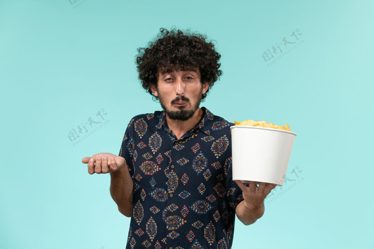 餐具正面图：年轻人拿着篮子 手里拿着土豆 站在蓝色的墙上看电影观看杯子容器