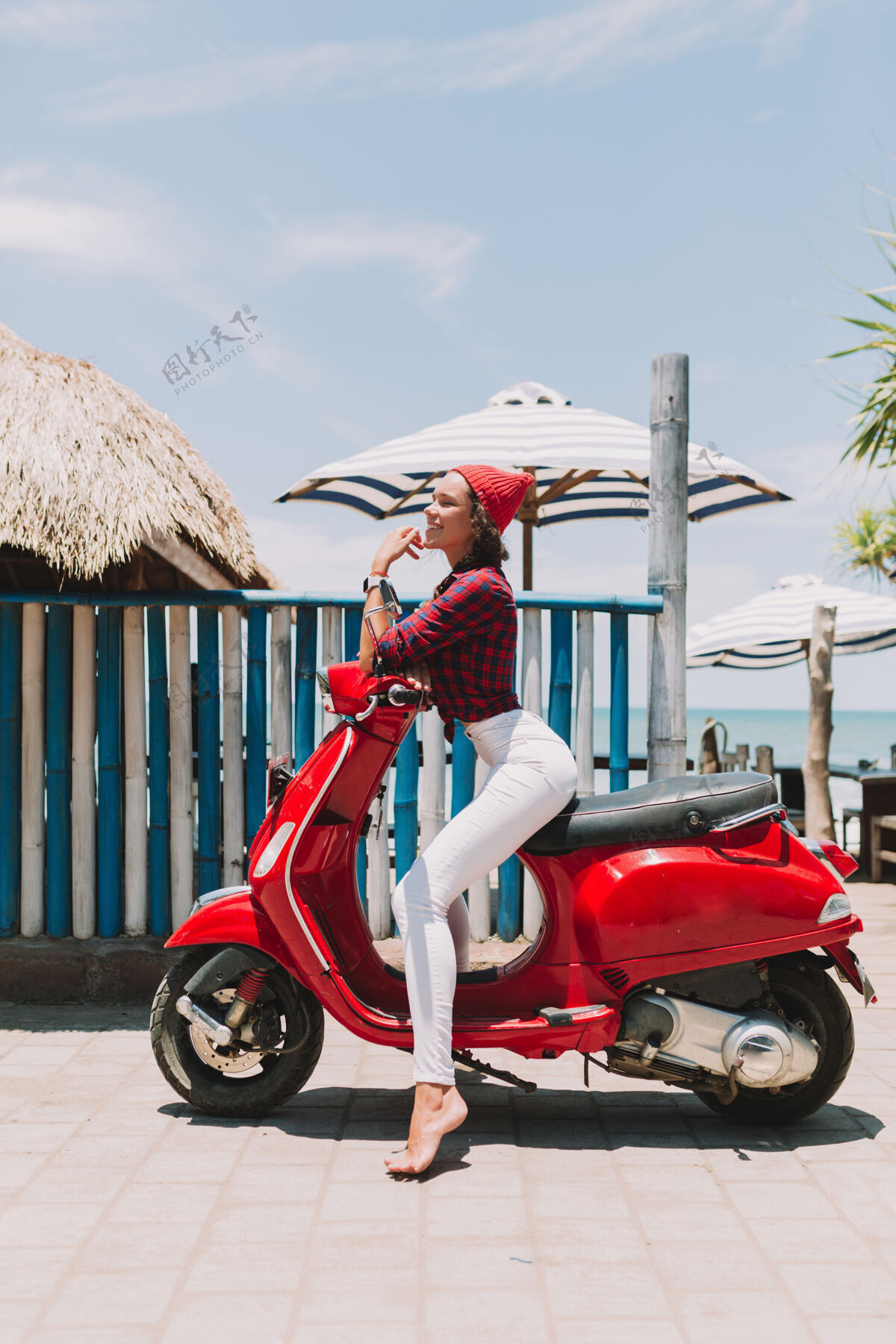 女士迷人时尚的年轻女子穿着白色裤子和衬衫 戴着太阳镜 坐在海边的红色摩托车上摆姿势女孩乐趣女性