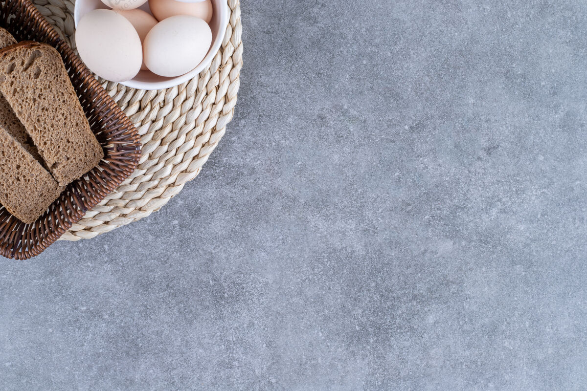 早餐柳条篮子的黑麦面包和一碗生鸡蛋放在石桌上家禽烹饪面包