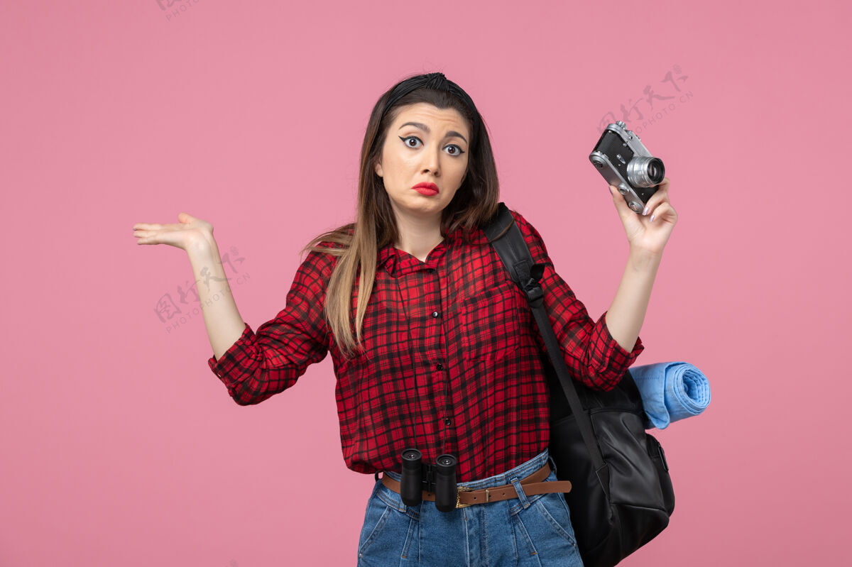 女士前视图穿着红色衬衫的年轻女性 在粉色背景上用相机拍照的女性模特表情人肖像
