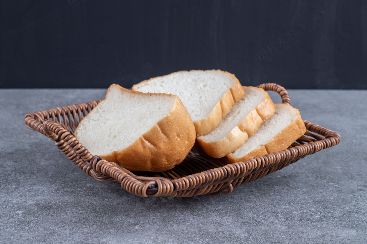 面包柳条篮子的切片白面包放在石头桌上吐司食欲面包屑