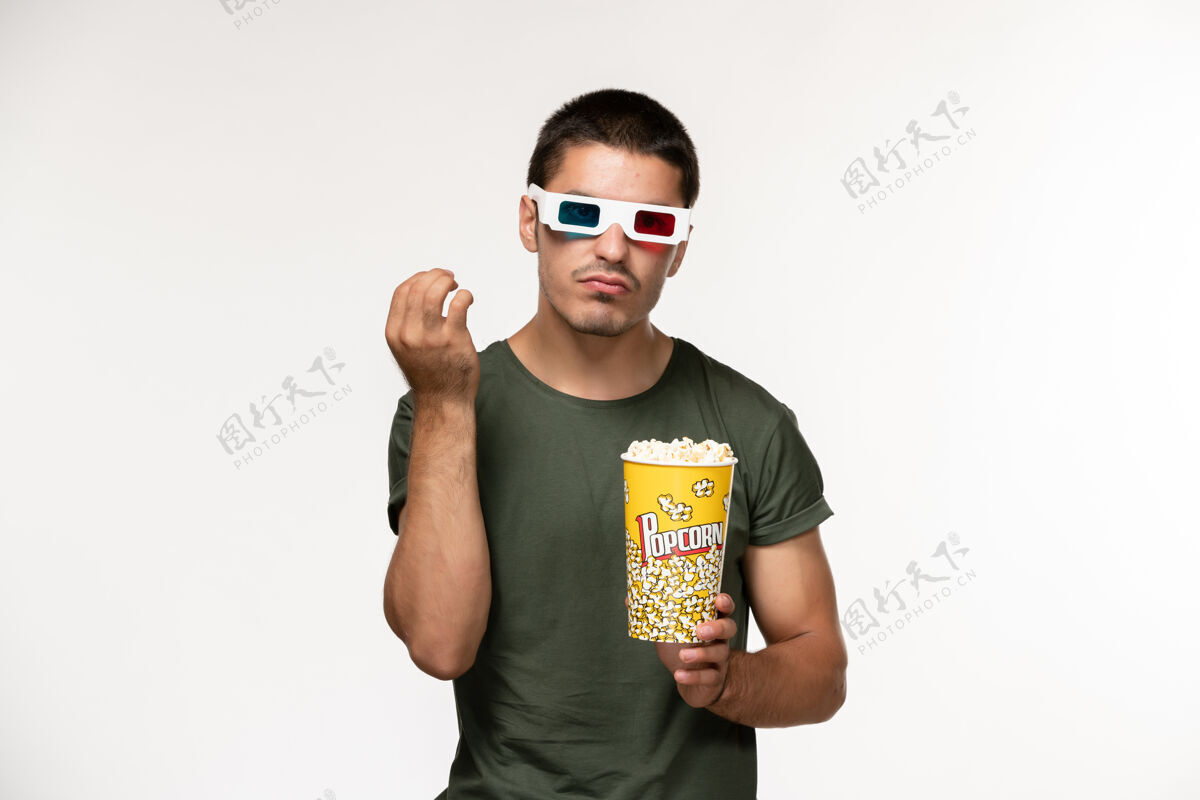 爆米花正面图身着绿色t恤 戴着d型太阳镜拿着爆米花的年轻男性在白墙上拍摄电影《孤独电影院》男性电影电影成人电影