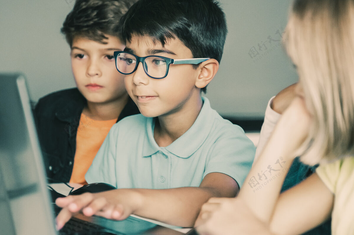 混合空间亚洲男孩在笔记本电脑键盘上打字 同学们坐在桌子旁 看着他一起做任务坐着人小学