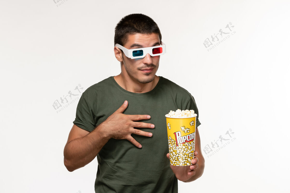电影正面图身穿绿色t恤的年轻男子戴着d型太阳镜拿着爆米花在白色办公桌上看电影孤独电影院男电影护目镜成人电影院